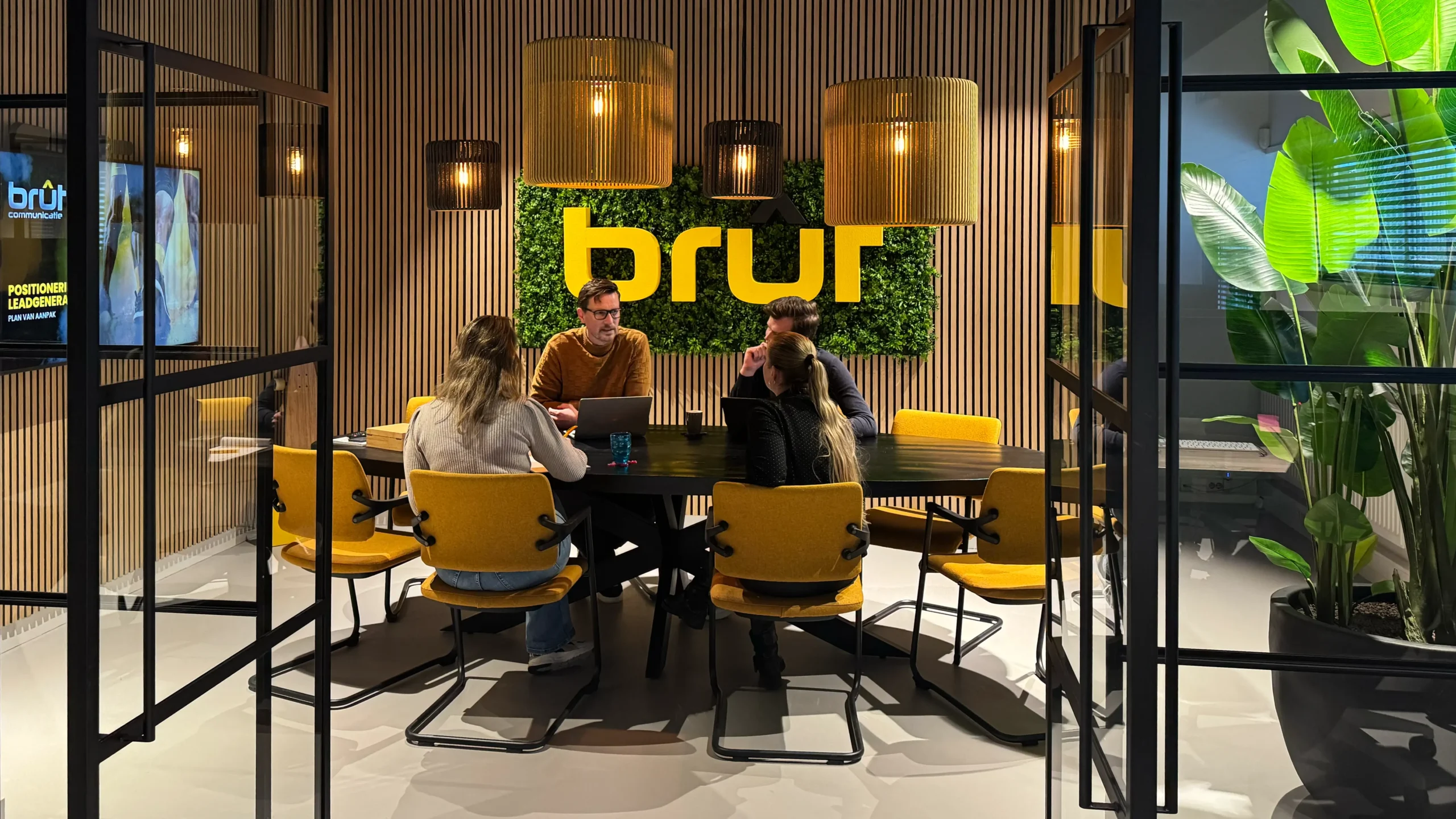 Vier mensen overleggen aan een ronde tafel in een moderne vergaderruimte met het logo van brut op de achtergrond
