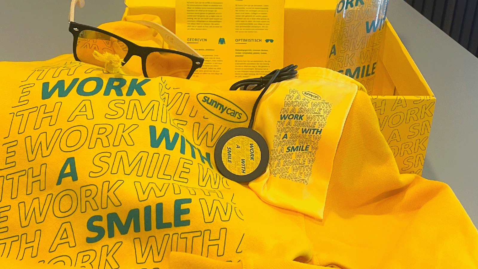 Sunnycars branding; gele doos gevuld met goodies als een zonnebril en andere merchandise.